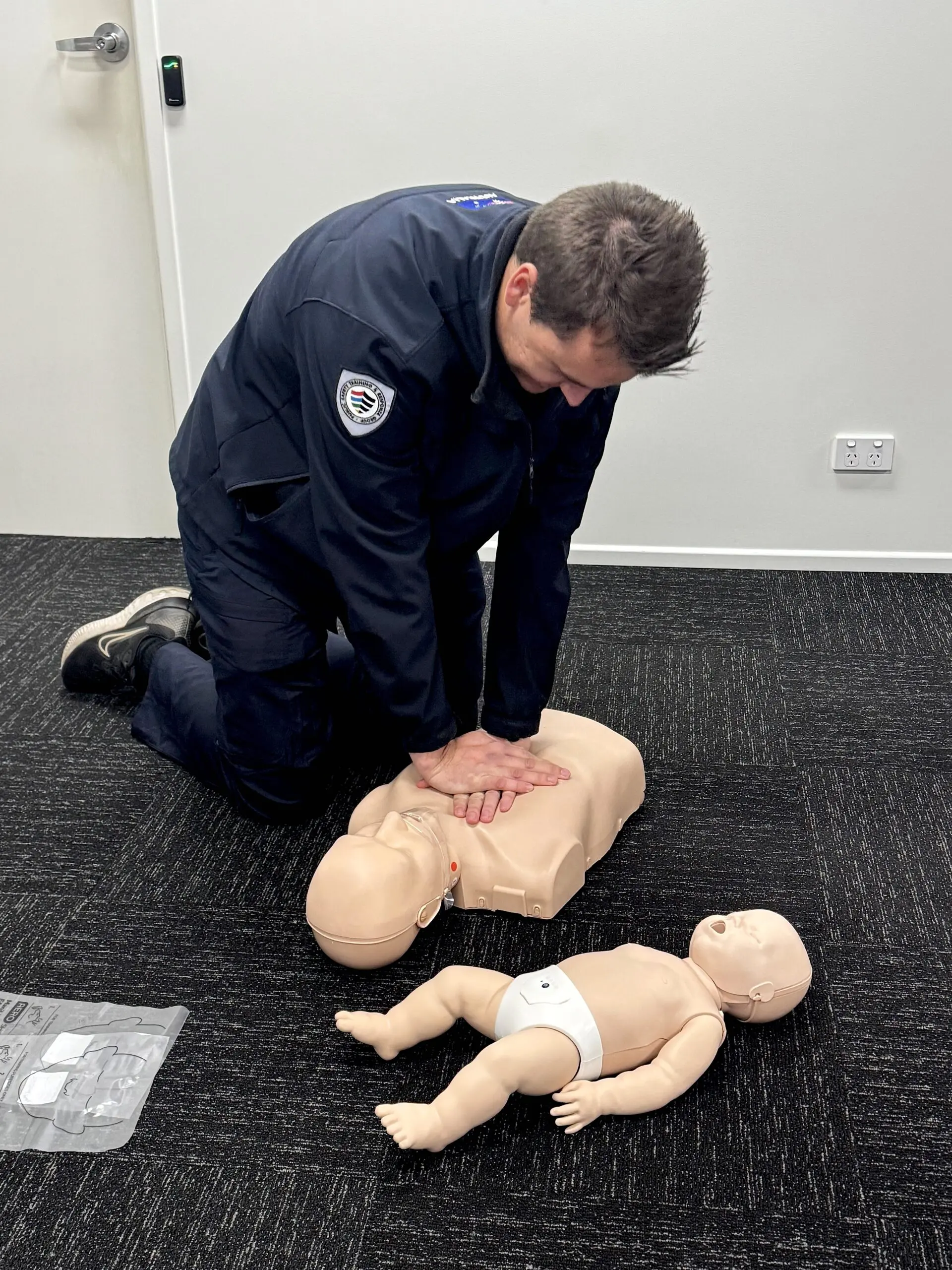 man dressed in black is practicing CPR on a baby mannequin.