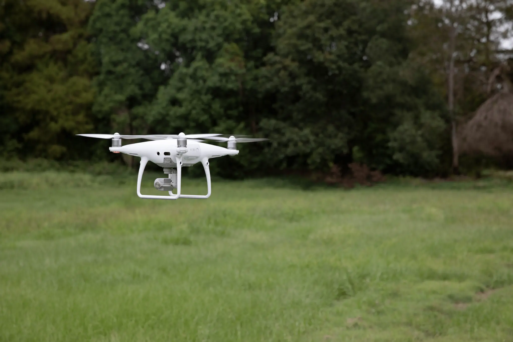 A white drone is hovering above the green forest.