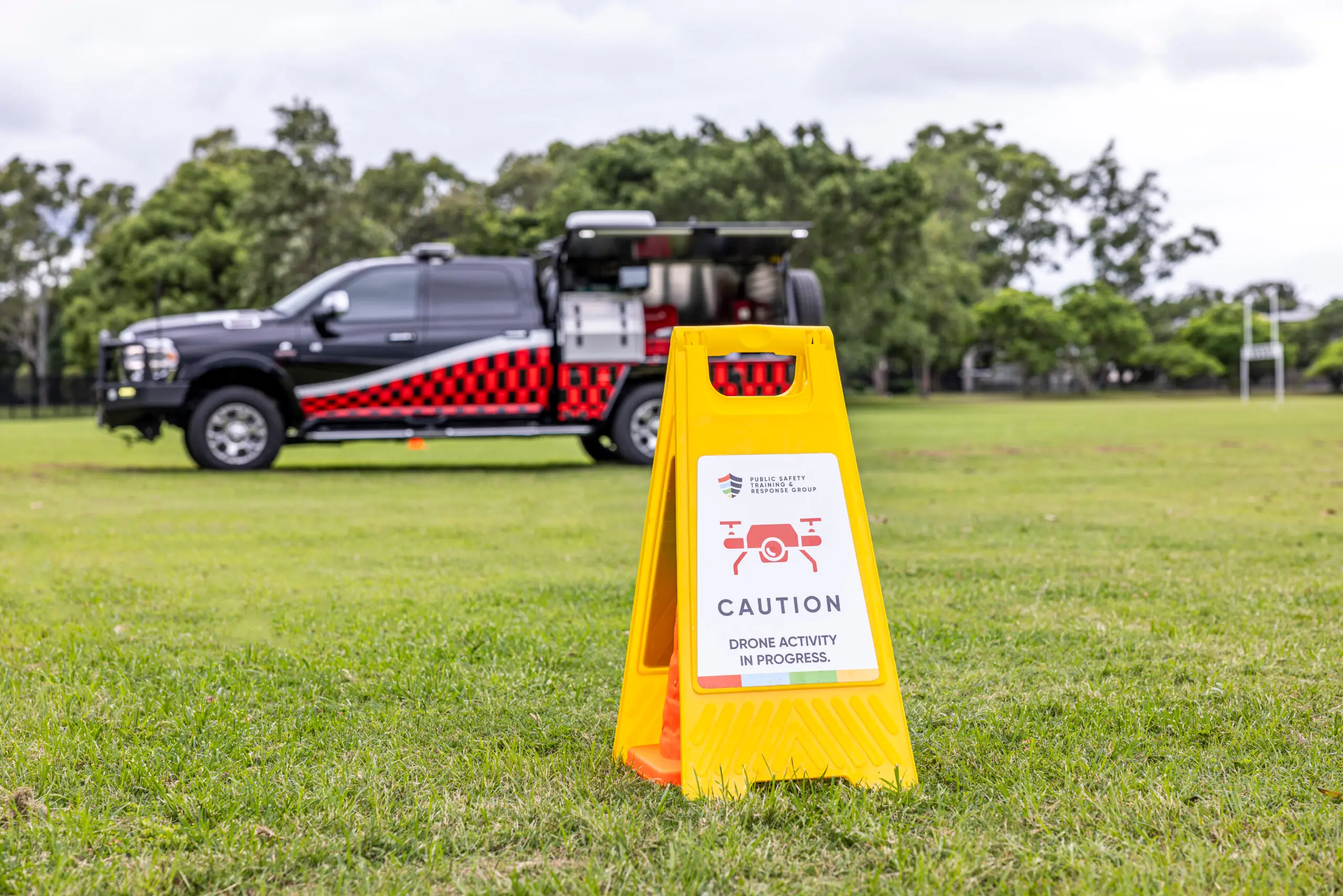 A yellow traffic cone stands on the grass in front of a black car