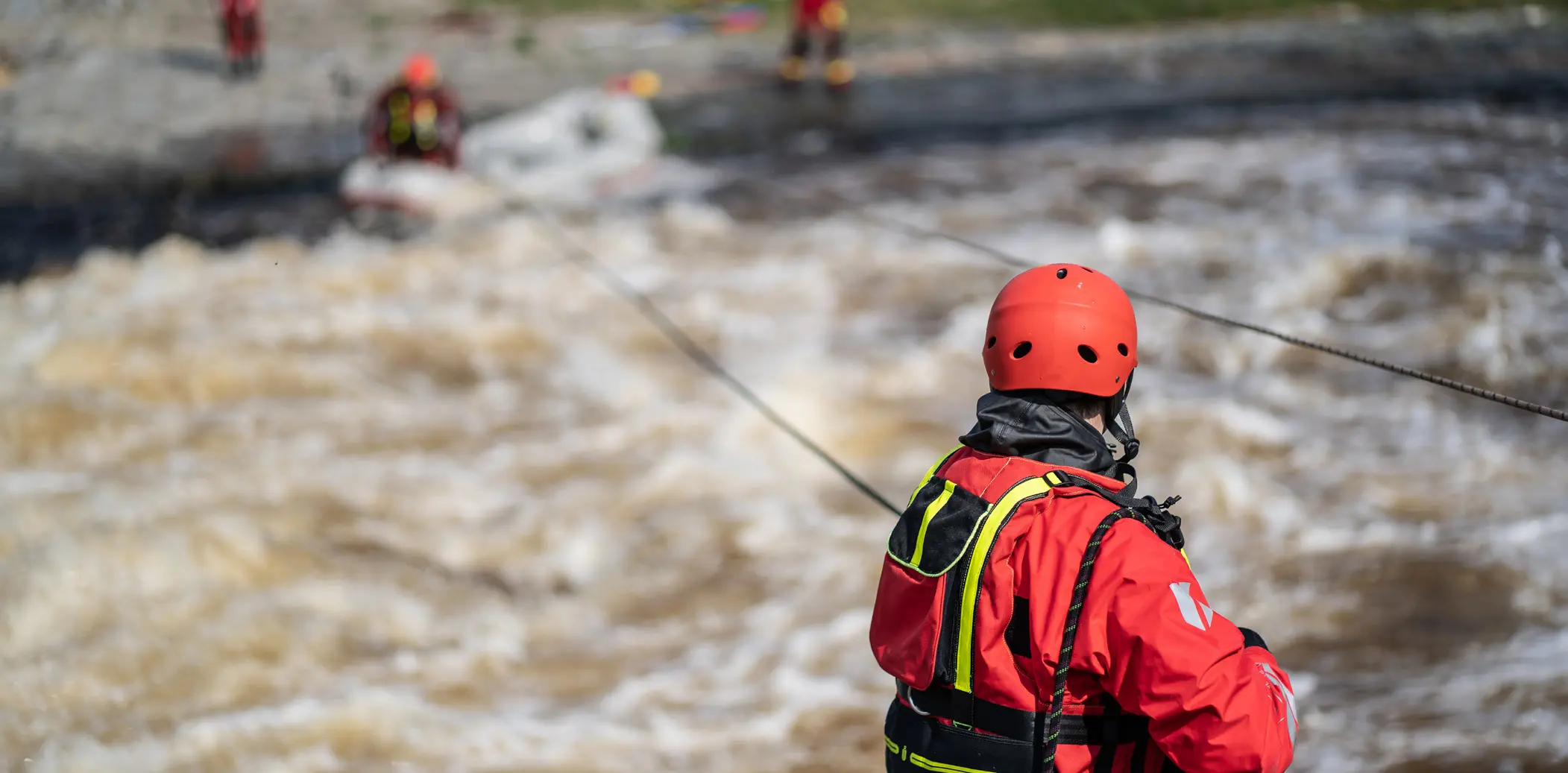 A man dressed in red is facing away, standing by a fast-flowing river