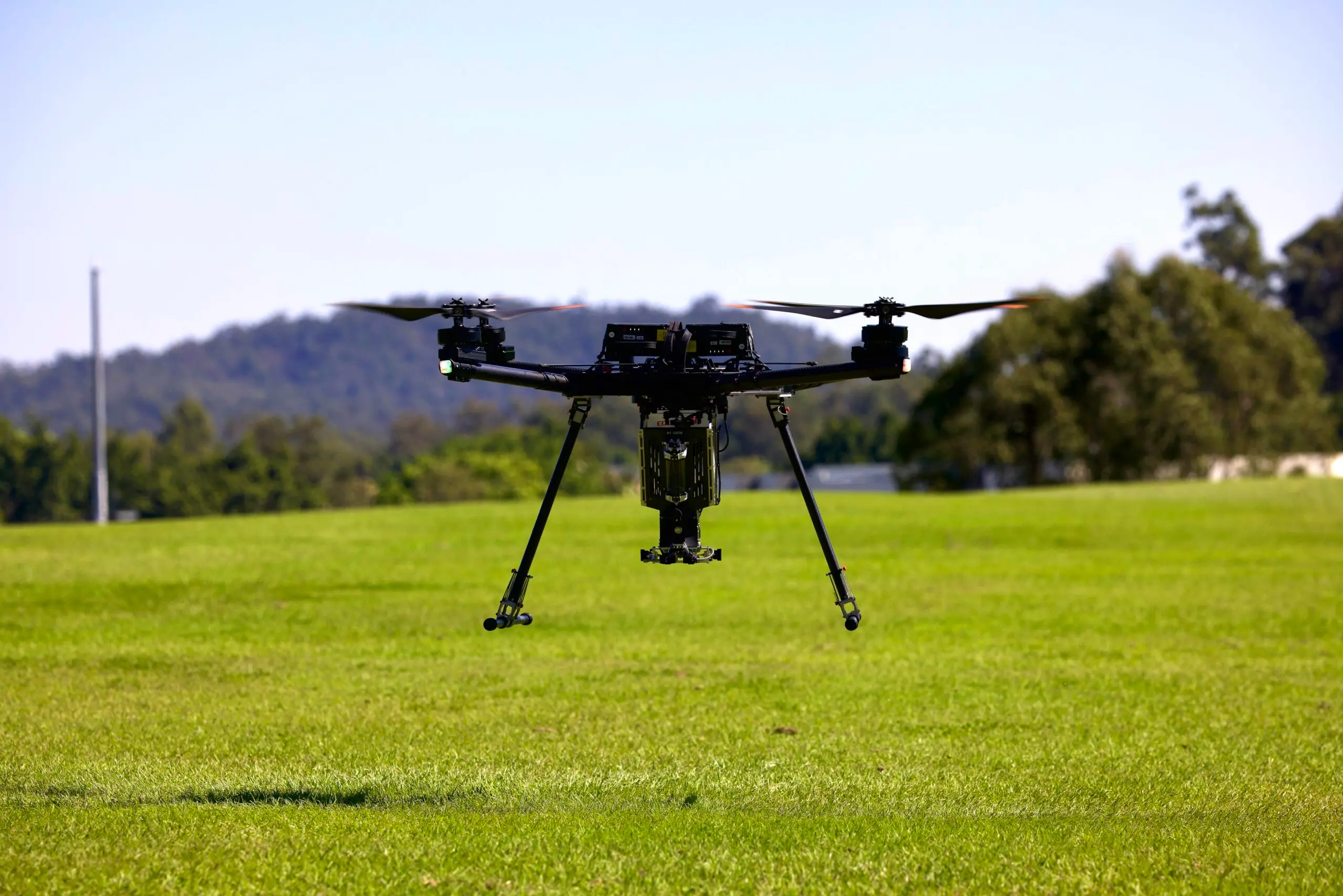 A black drone is touching down on a grassy surface